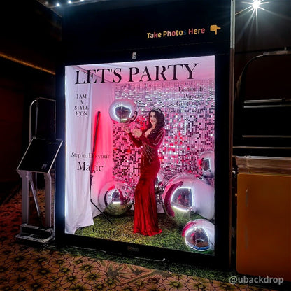 Black 6.5x7.5ft magazine photo booth with "LET'S PARTY" text, red dress model, sparkling sequin backdrop, and silver balloons.