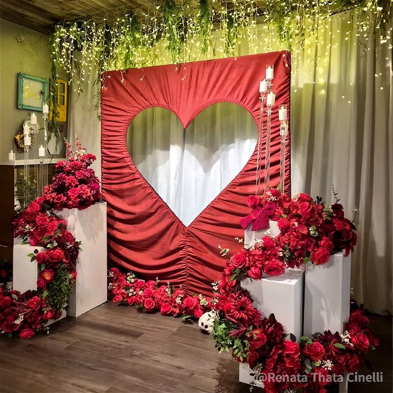 Elegant 6x6.8ft red ruched fabric backdrop stand with a heart cutout, surrounded by red roses and white pedestals.